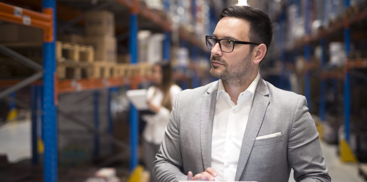 Portrait of successful businessman manager CEO holding tablet and walking through warehouse storage area looking towards shelves. Portrait of successful businessman manager CEO holding tablet and walking through warehouse storage area looking towards shelves.